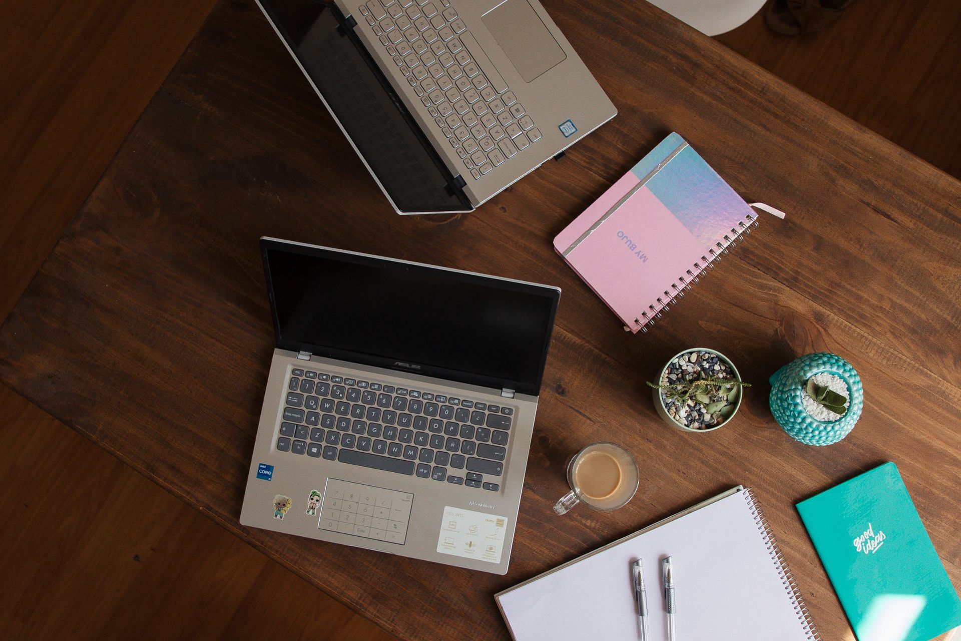 Dois laptops lado a lado sobre mesa de madeira, com cadernos coloridos, representando a escolha entre freelancer e agência de design