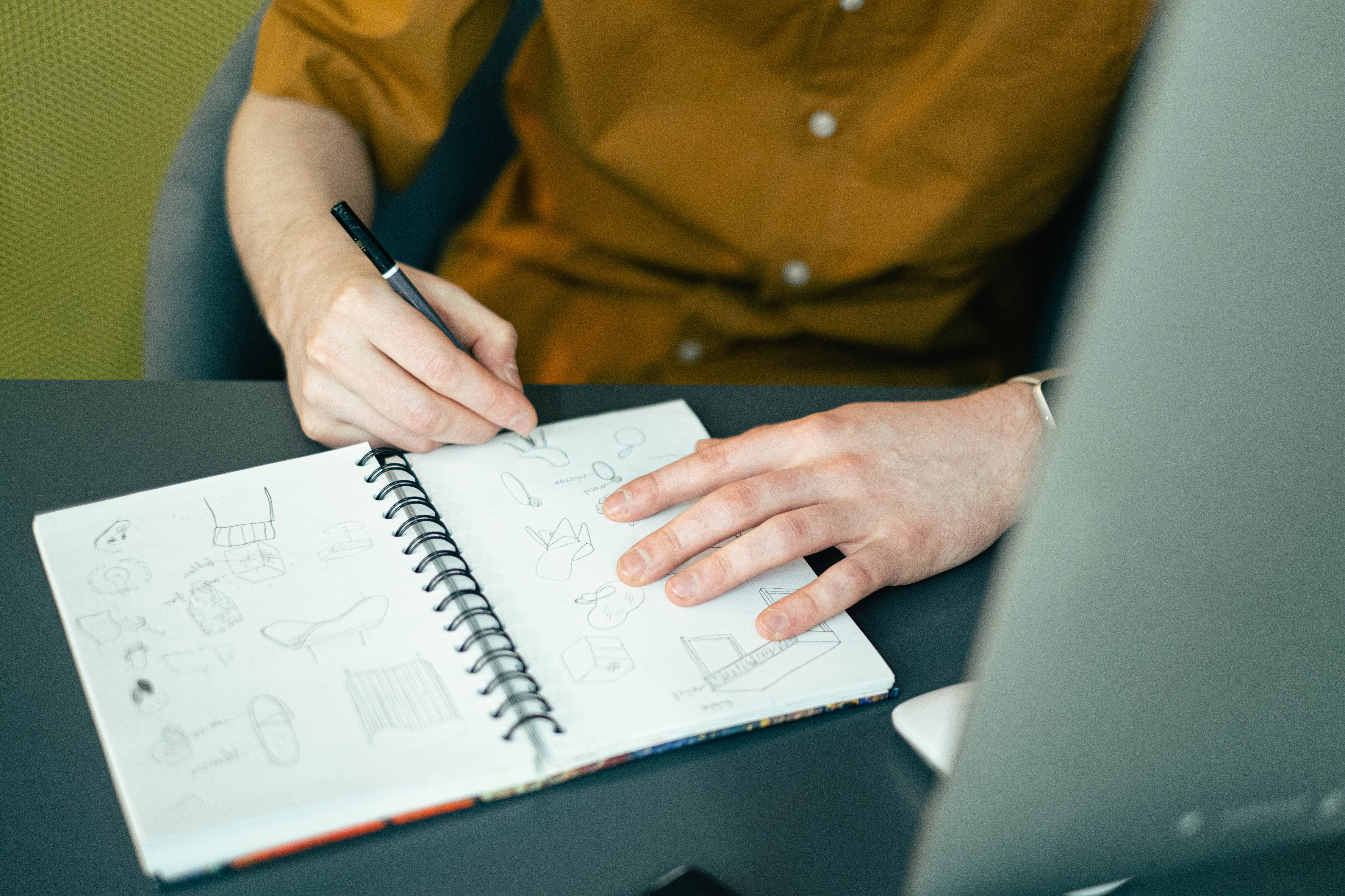 Designer esboçando ideias em um caderno de espiral sobre a mesa