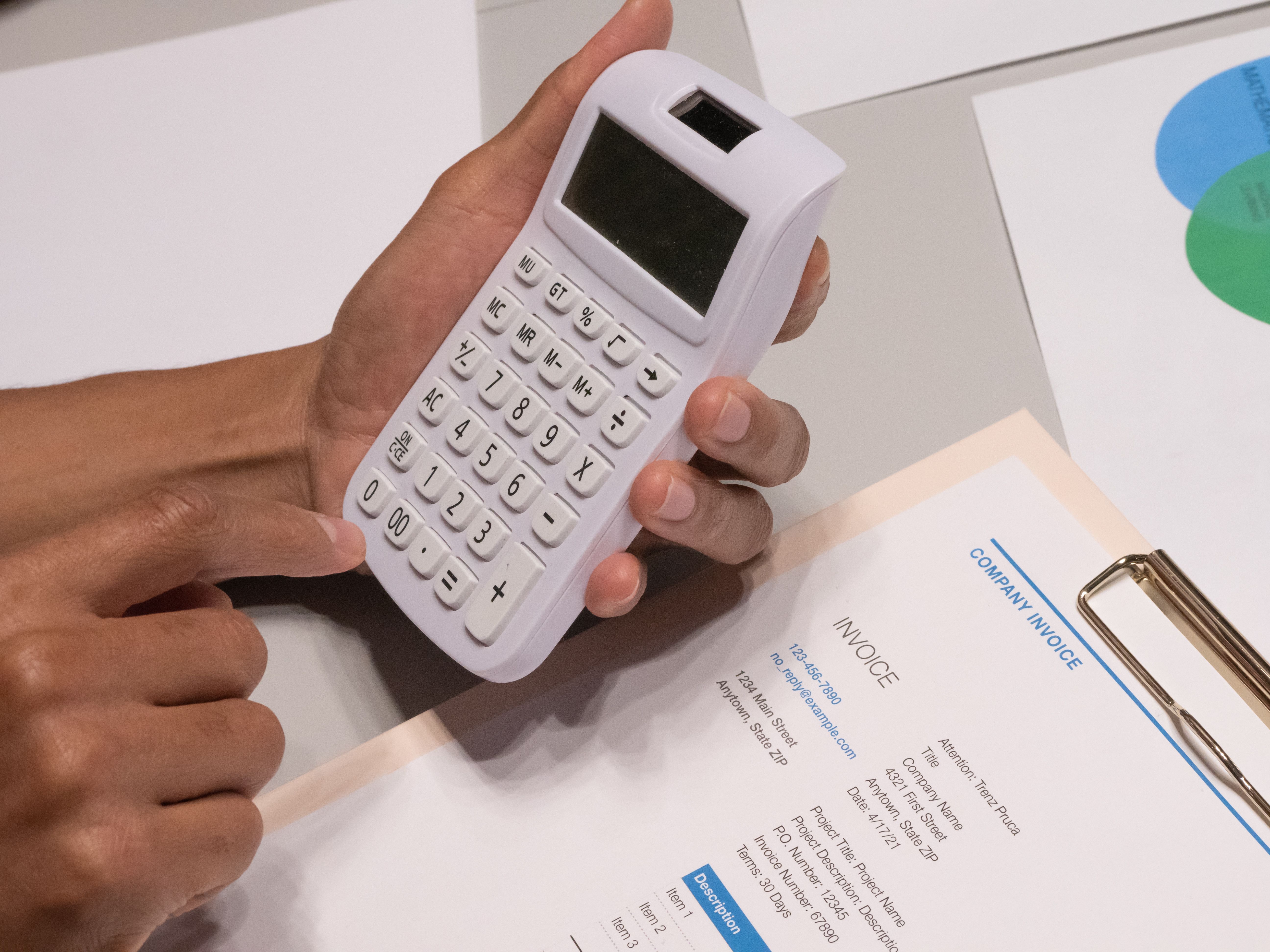 Close-up de mãos usando calculadora ao lado de uma nota fiscal, representando orçamento de um projeto